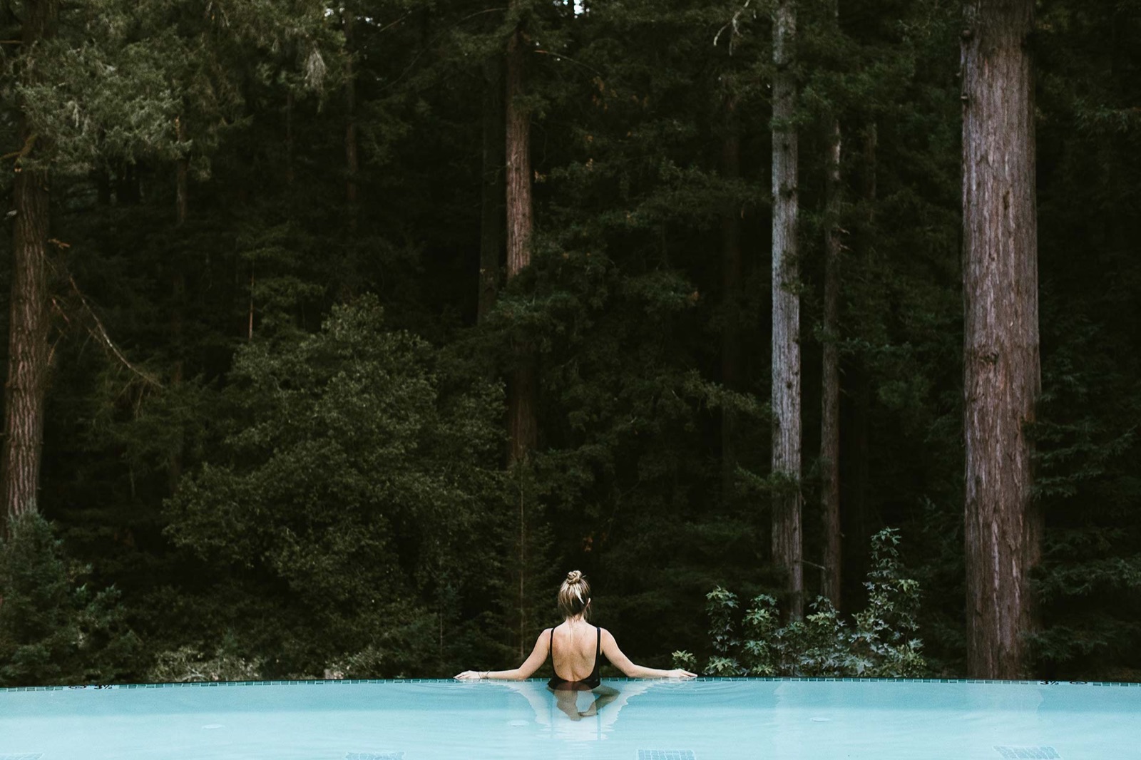 A guest relaxing in an infinity pool facing a redwood forest at 1440 Multiversity